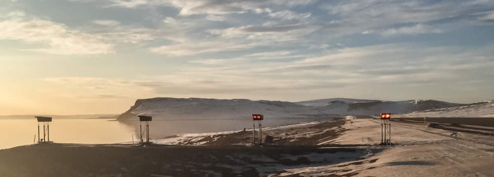 Beautiful view from a northern remote airport. Airfield lighting in the foreground, with snow-covered terrain and open water at dusk.