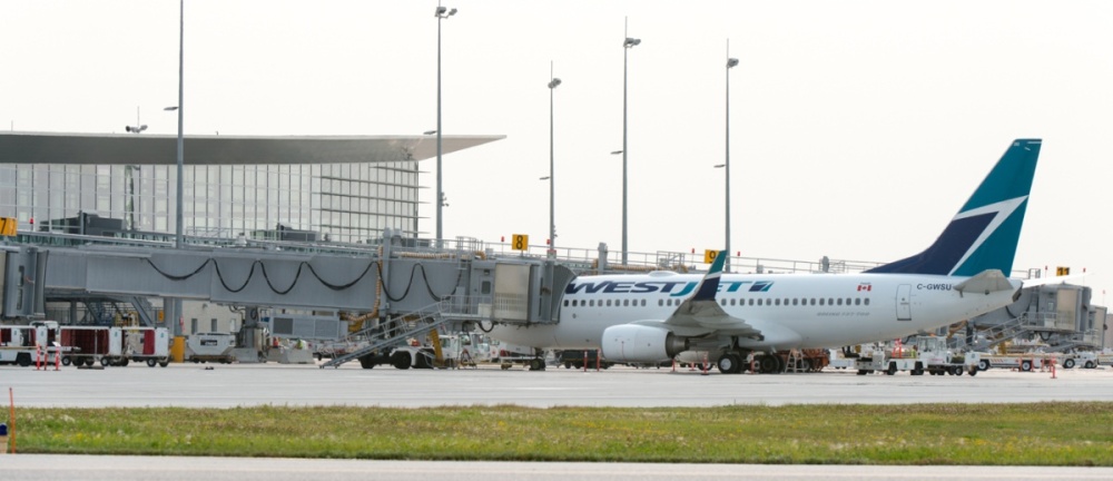 A plane sits at the gate of an airport, surrounded by airfield equipment.