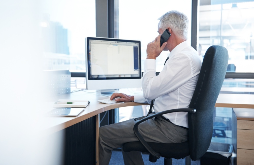 A man in business attire is sitting at a desk, talking on the phone.