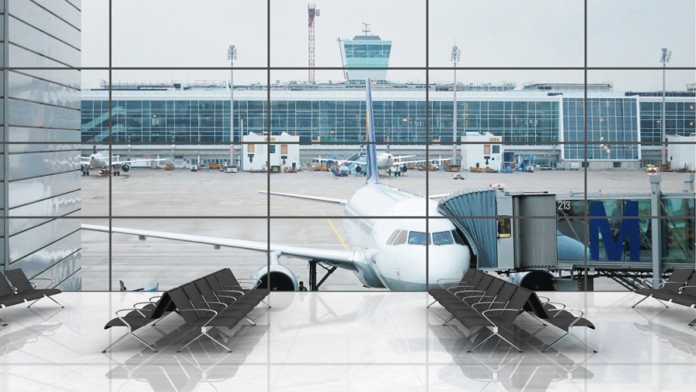 Photo of a waiting area in an airport terminal building. Out the window, a plane sits at the gate surrounded by airfield equipment.