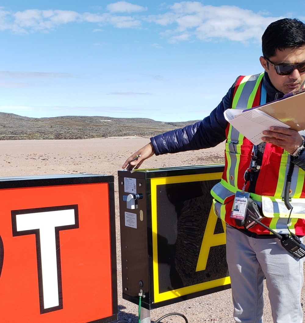 A WASCO employee holds a clipboard and inspects airfield signage.