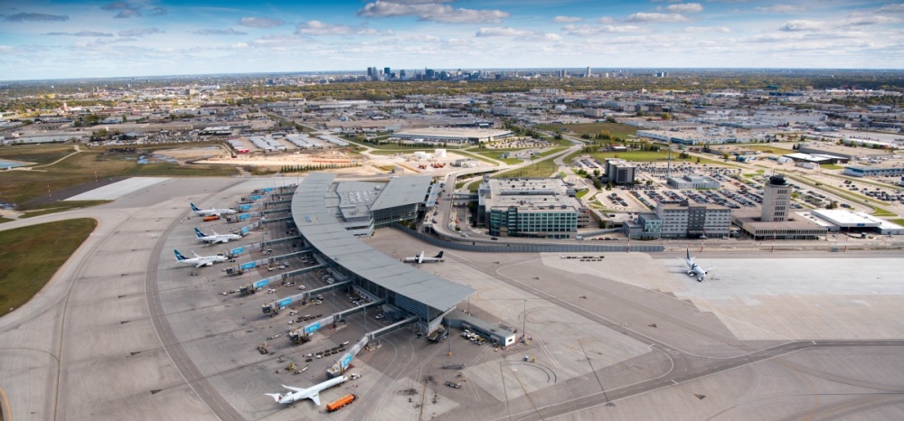 An aerial view of an airport and airfield surrounded by commercial property and the city's downtown in the background.