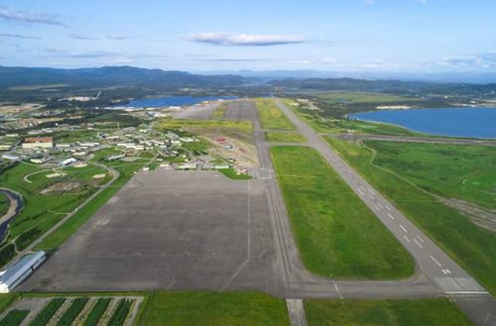 Aerial view of Stephenville airport and runways, with green fields to the left, ocean to the right, and mountains in the background.