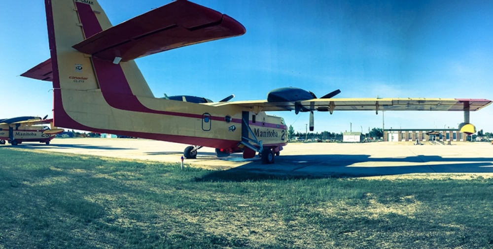 Photo of an old plane in the foreground, with The Pas Airport in the background.